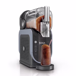 A hand pouring red juice into the easy-fill transparent top vessel of a Ninja frozen drink maker on a kitchen counter. The text emphasizes that the vessel is easy to fill, top off, and clean.