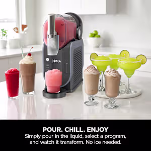 A Ninja slushie machine on a bright kitchen counter surrounded by freshly made frozen drinks, including red slushies, chocolate frappes, and green margaritas. The text highlights "Pour. Chill. Enjoy. No ice needed."